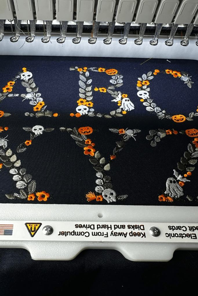 Floral Halloween Alphabet letters stitched out on navy fabric, still hooped on the machine