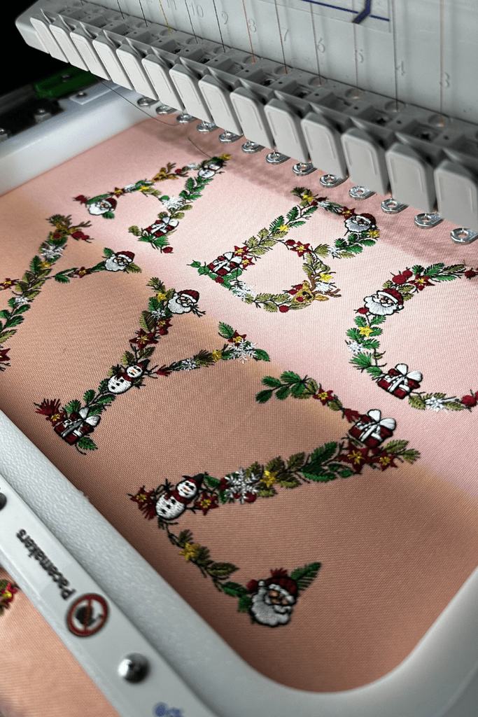 Floral Christmas Alphabet letters stitched out on pink fabric, still hooped on the machine