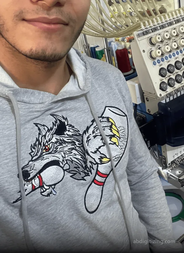machine emboridery of a wolf holding a bowl with the claws on a grey jacket